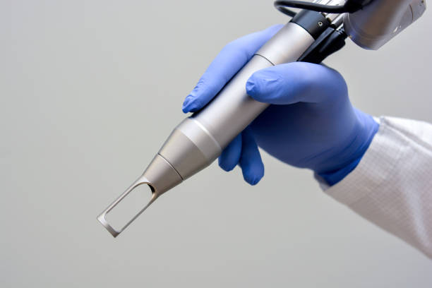 Gros plan sur la main d'un médecin tenant une pièce à main laser épilation maillot ND:Yag sur fond gris.